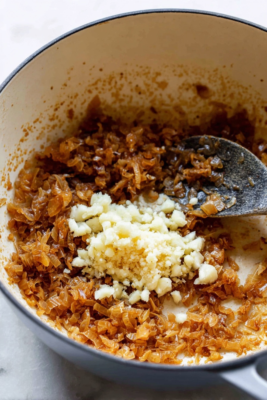 The image shows a white pot with a round shape filled with a mix of browned, soft, finely chopped onions that have a caramelized light brown color and a soft texture. On top of the onions, there is a small pile of finely chopped fresh garlic with a pale off-white color and a slightly rough texture. A metal spoon with a dark handle is partially visible, stirring the mixture inside the pot. The inside of the pot has some browned spots from cooking, enhancing the rich look of the onions and garlic. The pot rests on a white marbled surface. Photo taken with an iphone --ar 2:3 --v 7