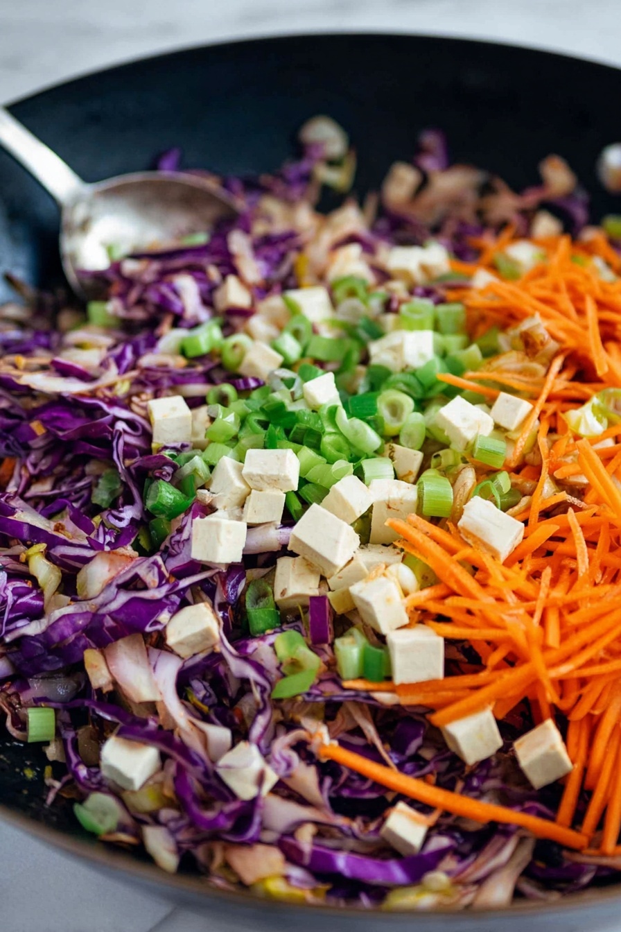 This image shows a close-up of a stir-fry mix in a black pan with different colorful ingredients. The base layer has shredded purple cabbage with a bright, smooth texture and thin strips. On top of the cabbage is a layer of thin, orange carrot strips that add brightness and freshness. Scattered evenly among the cabbage and carrot are small, cubed white tofu pieces adding a soft and firm contrast. There are also chopped green onion slices spread throughout, offering a fresh green color and a slightly crisp texture. The ingredients look lightly cooked but still fresh, and a metal spoon is partially visible stirring the mix. The background has a white marbled texture photo taken with an iphone --ar 2:3 --v 7